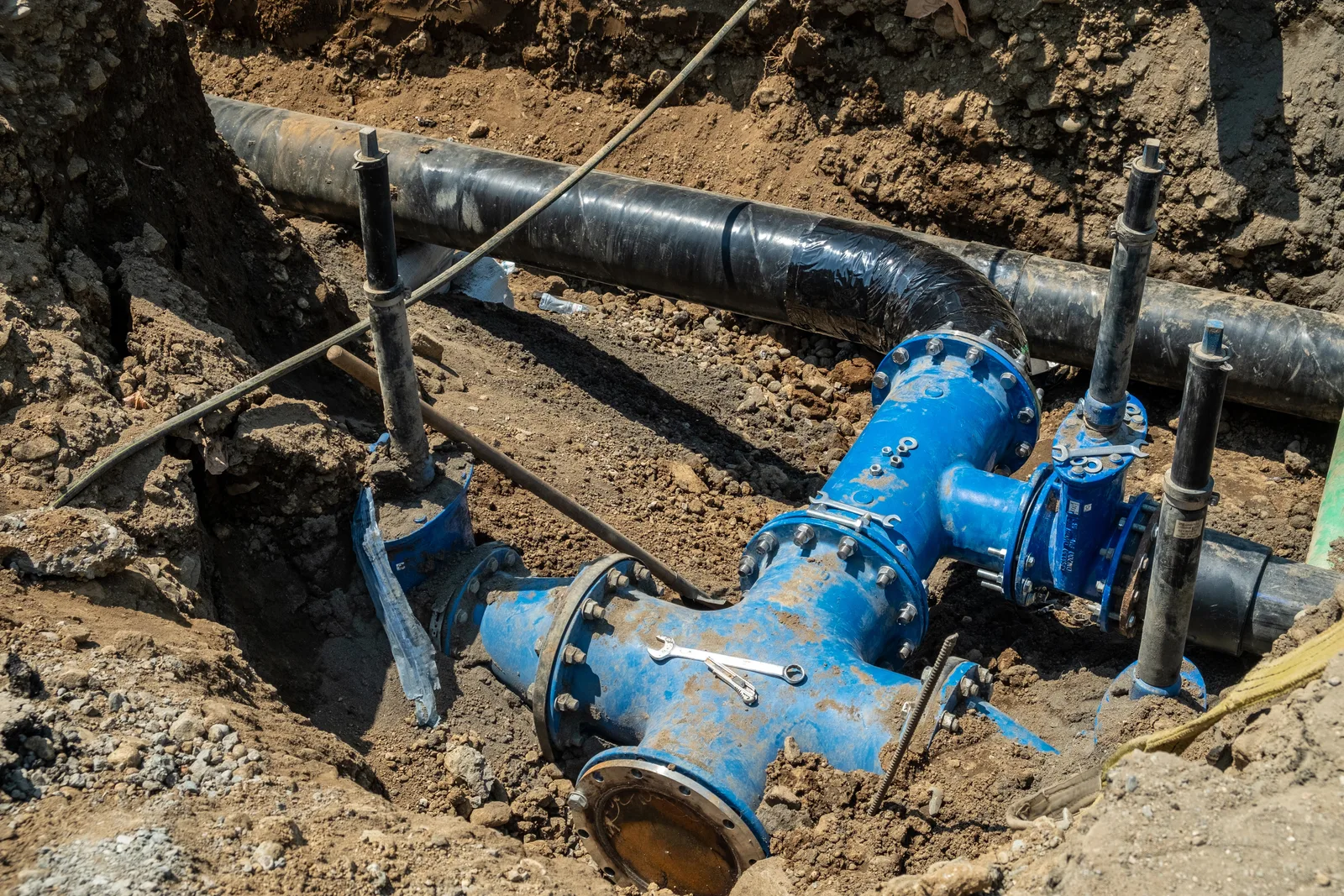 Blue water mainlines and valves connected in a dirt trench.